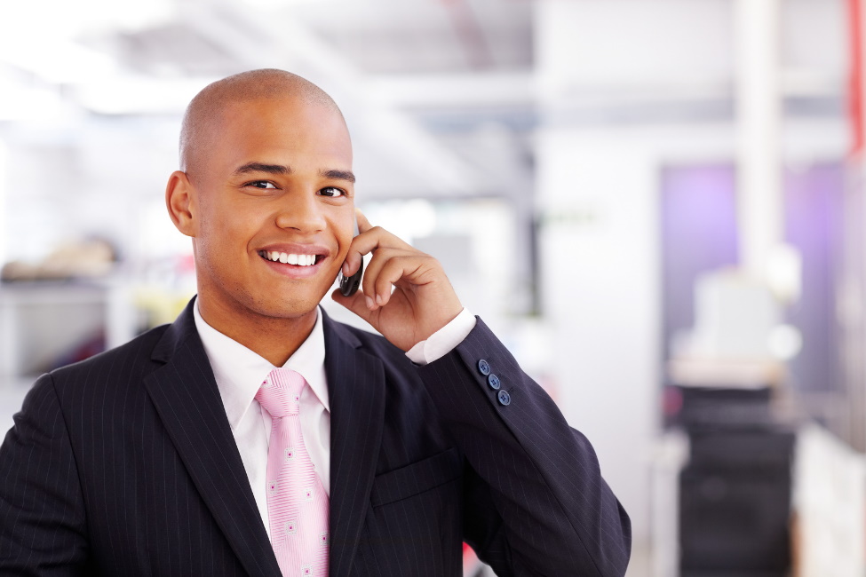 businessman facing the camera and smiling, holding a smartphone to his ear